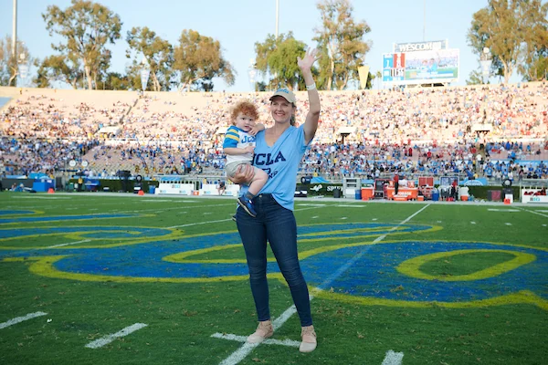 Vanessa Teff holding her son on the field at the Rose Bowl